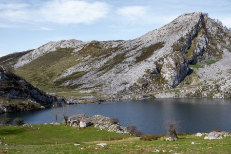 Foto de Lagos de Covadonga, una imponente montaña con un tranquilo lago enclavado en su centro, rodeado por la grandeza de los Picos de Europa en el fondo. - Imagen libre de derechos