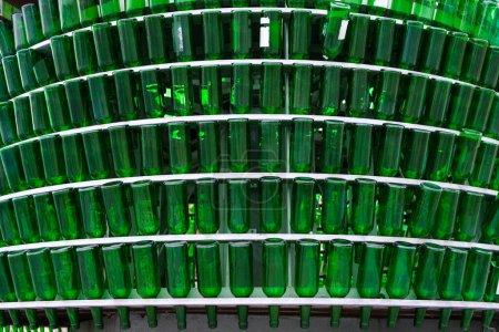 Une importante collection de bouteilles en verre vert soigneusement empilées sur une étagère, probablement en attente de recyclage industriel ou de réutilisation. Les bouteilles apparaissent uniformes dans la forme et la couleur, créant une vue saisissante.