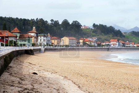 A group of individuals walking along a sandy beach in Ribadesella, Asturias, Spain. The group is strolling casually, enjoying the seaside scenery on a sunny day.