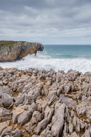 Foto de Una vista de una playa rocosa con rocas afiladas que sobresalen del agua en Los Bufones de Llanes, Asturias. Las olas chocan contra la escarpada costa, creando una escena dinámica y poderosa. - Imagen libre de derechos