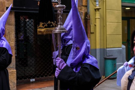 Foto de Nazarenos, Persona vestida con una túnica púrpura sostiene una copa de plata mientras participa en una procesión de Nazarenos con traje tradicional español de Pascua. - Imagen libre de derechos