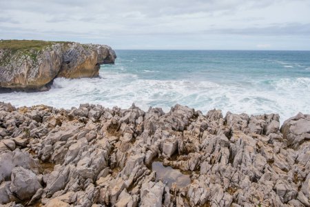 Foto de Una vista de la escarpada costa rocosa de Los Bufones de Llanes, Asturias, con rocas afiladas que sobresalen en el extenso cuerpo de agua. - Imagen libre de derechos