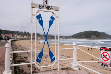 Ein Schild im Sand an einem Strand, an dem zwei blaue Kajaks befestigt sind. Die Kajaks sind sicher befestigt und für Strandbesucher einsatzbereit.