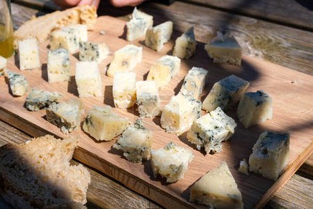 Una tabla de cortar de madera está cubierta con un surtido de queso Cabrales, mostrando una variedad de texturas y colores. El queso está rebanado y arreglado cuidadosamente, listo para degustar.