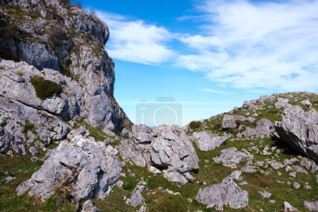 Un paysage avec des roches faites de roches calcaires et des plaques d'herbe sous un ciel bleu clair. Les rochers sont éparpillés sur le sol, avec des touffes d'herbe verte qui poussent entre les deux.