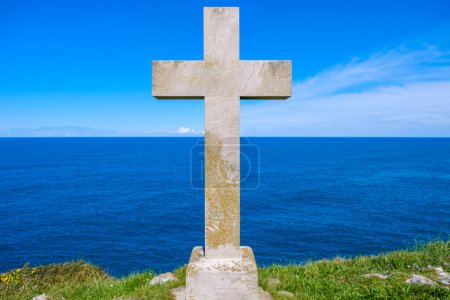 Foto de Una cruz cristiana está de pie en una colina, proyectando una sombra sobre el fondo del vasto océano con olas que se estrellan debajo. La escena emana un sentido de solemnidad y reverencia. - Imagen libre de derechos
