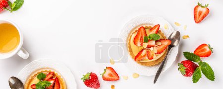 Photo for Banner with small tartlet pastries with vanilla custard, topped with strawberry fruits and almond sprinkles and tea over white background. Concept of homemade sweet pastries. Copy space, top view - Royalty Free Image
