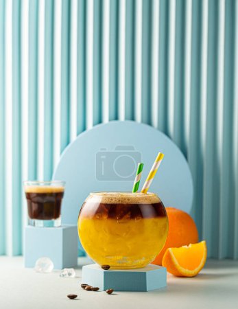 Photo for Bumble coffee with ice on blue background. Espresso, orange juice and syrup in layers in transparent glass with ice. Summer trendy refreshing coffee drink. Copy space - Royalty Free Image