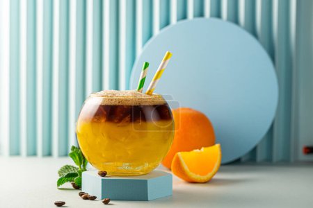 Photo for Bumble coffee with ice on blue background. Espresso, orange juice and syrup in layers in transparent glass with ice. Summer trendy refreshing coffee drink. Copy space - Royalty Free Image