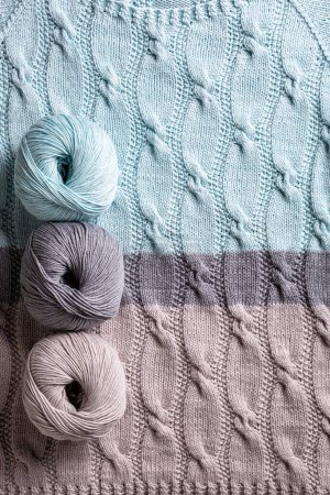 Photo for Cotton cashmere balls yarn over abstract turquoise gray knitted pattern background texture with cables. Top view of knitting clothes - Royalty Free Image