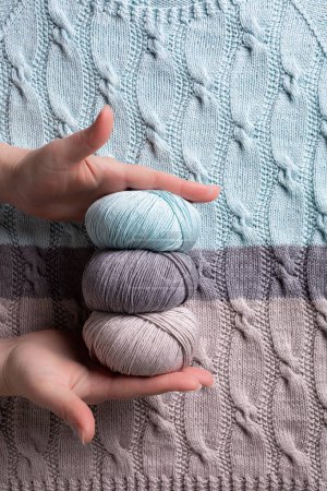 Photo for Female hands with cotton cashmere balls yarn over abstract turquoise gray knitted pattern background texture with cables. Top view of knitting clothes - Royalty Free Image