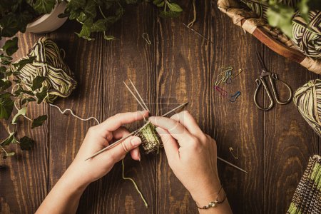 Photo for Female hands knitting green socks in progress. Flat lay on wooden table with coffee and house plants, copy space, top view. - Royalty Free Image