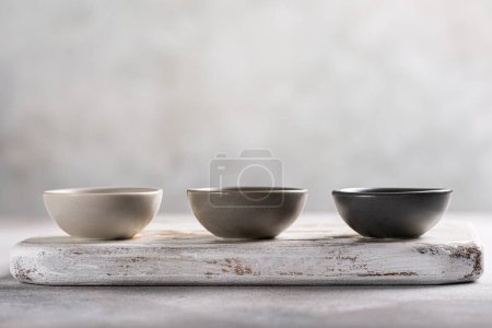 Photo for Three empty gray small bowls on old white wooden board. Mini plates for sauce or dip. Copy space - Royalty Free Image