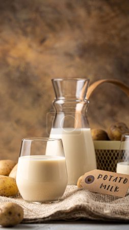 Photo for Vegan plant based milk in transparent glass. Alternative potato milk and potato tubers on sackcloth. Healthy vegetarian and vegan drink concept with copy space. Smartphone format for phone wallpaper - Royalty Free Image