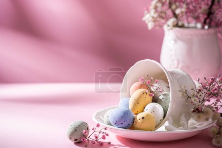 Photo for White porcelain coffee cup with colorful quail eggs and spring flowers over pink background. Springtime and Easter holiday concept with copy space - Royalty Free Image