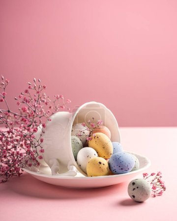 Photo for Easter composition with spring flowers and colorful quail eggs in porcelain white coffee cup over pink background. Springtime and Easter holiday concept with copy space - Royalty Free Image