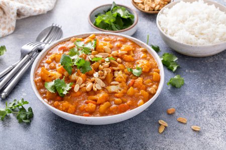 Foto de Curry vegano con coliflor, garbanzos y calabaza rematada con maní, servido con arroz y cilantro - Imagen libre de derechos