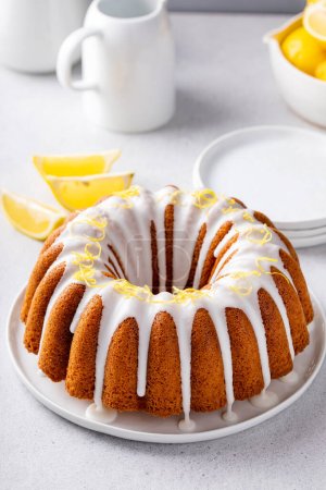 Lemon bundt cake drizzled with powdered sugar glaze topped with lemon zest on a plate