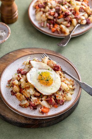 Corned beef hash with potatoes, cabbage and carrot on a plate topped with a fried egg