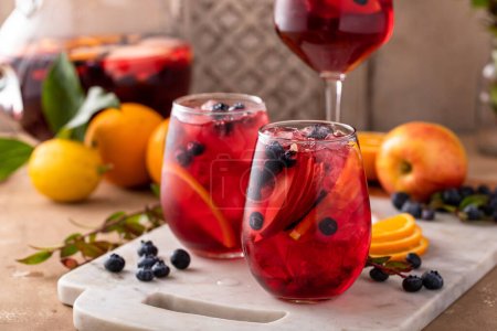 Foto de Refrescante sangría de bayas de verano con manzanas, naranjas y arándanos en copas de vino con hielo - Imagen libre de derechos