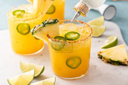 Photo for Pineapple spicy margarita cocktail in glasses with chili tajin rim, jalapenos and a slice of pineapple, refreshing summer cocktail - Royalty Free Image