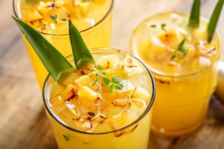 Photo for Grilled pineapple cocktail or mocktail in tall glasses garnished with pineapple leaves, refreshing summer drink idea - Royalty Free Image