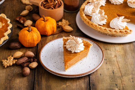 Téléchargez les photos : Tarte à la citrouille traditionnelle pour Thanksgiving avec crème fouettée et décorations en forme de feuille avec une tranche retirée - en image libre de droit