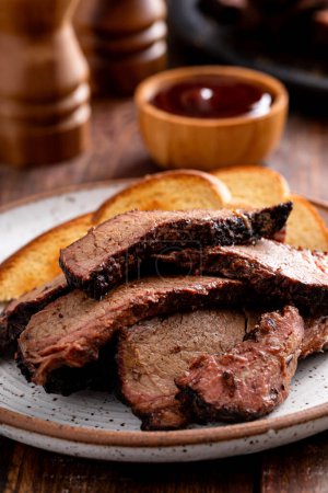 Sliced smoked brisket on a plate with toast served with BBQ sauce