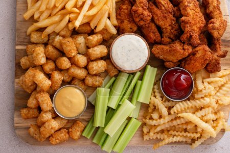 Fried chicken strips and french fries board with sauces and celery, fast food snack board idea