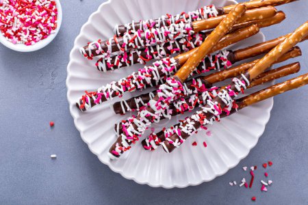 Schokolade eingetauchte Brezelstangen mit dunkler und weißer Schokolade und rosa Herzstreuern auf einem Teller