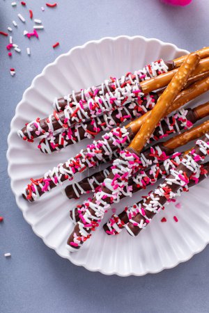 Chocolate dipped pretzel rods with dark and white chocolate and pink heart sprinkles on a plate