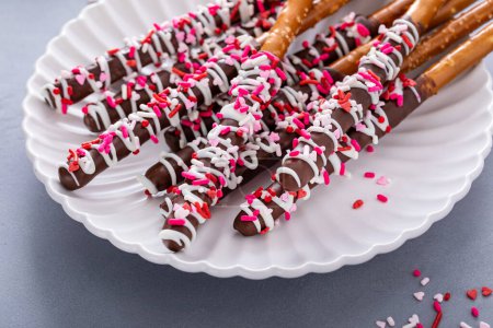 Schokolade eingetauchte Brezelstangen mit dunkler und weißer Schokolade und rosa Herzstreuern auf einem Teller