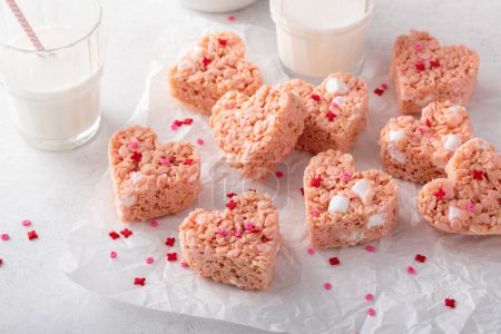 Rosado corazón en forma de arroz krispie golosinas cubiertas con aspersiones servidas con leche, dulce casero para el Día de San Valentín