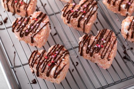 Pink heart shaped rice krispie treats drizzled with dark chocolate on a cooling rack, homemade sweet treat for Valentines Day