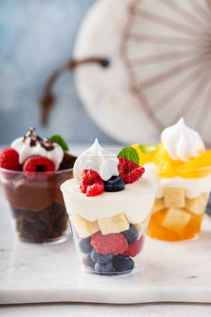 Three desserts in cups, variety of trifles with orange, chocolate and berry cakes