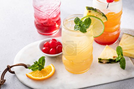 Tropische Tiki-Cocktails in lustigen Tiki-Gläsern, garniert mit Fruchtscheiben und Minzblättern
