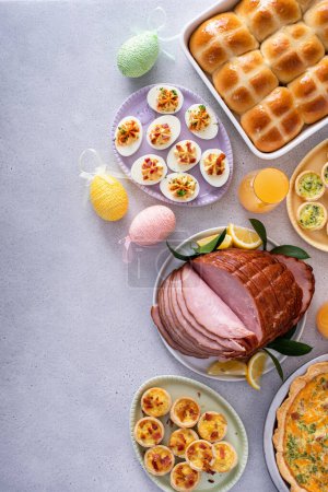 Easter brunch on large table with spiral sliced ham, quiche, deviled eggs and hot cross buns with Easter decor with copy space