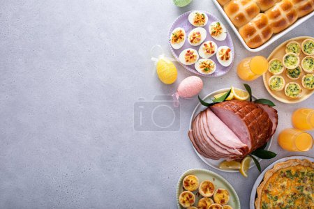 Easter brunch on large table with spiral sliced ham, quiche, deviled eggs and hot cross buns with Easter decor with copy space