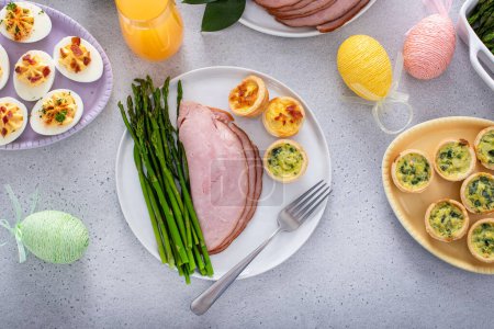 Easter brunch table with a potion of ham with asparagus on the plate with mini quiches