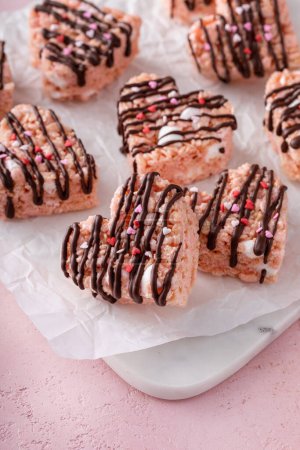 Pink heart shaped rice krispie treats drizzled with dark chocolate on a cooling rack, homemade sweet treat on a marble board