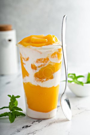Téléchargez les photos : Smoothie à la mangue avec crème de coco fouettée tourbillonnée dans une grande tasse, collation rafraîchissante ou dessert sain pour le petit déjeuner - en image libre de droit
