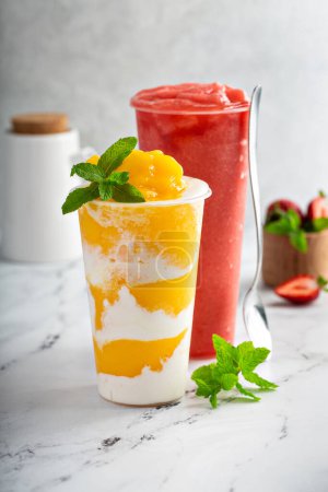 Téléchargez les photos : Smoothie à la mangue avec crème de coco fouettée tourbillonnée dans une grande tasse et smoothie à la pastèque aux fraises - en image libre de droit