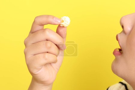 Téléchargez les photos : La femme asiatique mangeant du pop-corn de la main sur le fond jaune. - en image libre de droit