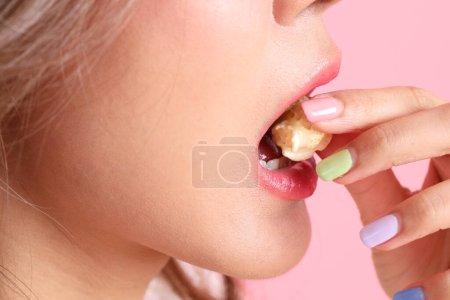 Téléchargez les photos : La femme asiatique mangeant du pop-corn de la main sur le fond rose. - en image libre de droit