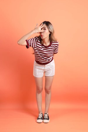 The young Asian woman in casual clothes with gesture of smelling, cover nose on the orange background 