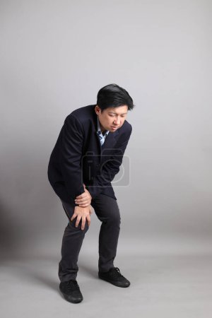 The Asian Businessman with formal dressed  with gesture of exhausted on the gray background.