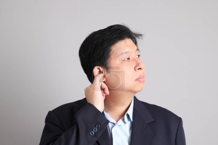 Der asiatische Geschäftsmann mit formalen gekleidet mit Geste der Faulheit und unernst auf dem grauen Hintergrund.