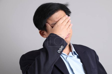 El empresario asiático con formal vestido con gesto de agotado sobre el fondo gris.