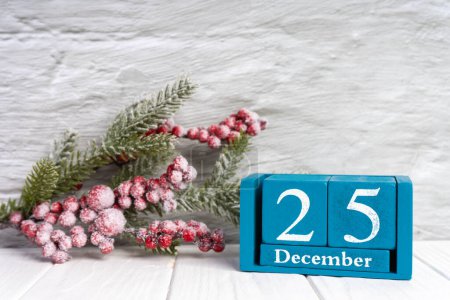 Foto de Rama de árbol de Navidad con bayas rojas y calendario perpetuo azul con fecha 25 diciembre en la pared de ladrillo blanco. Banner, encabezado, fondo de Año Nuevo - Imagen libre de derechos