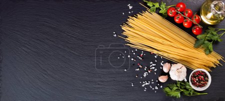 Foto de Pasta, espaguetis e ingridientes para cocinar en la superficie de pizarra negra. Concepto de cocina italiana, menú de restaurante, plantilla de receta. Vista superior, plano, maqueta, banner, encabezado con espacio de copia para el texto - Imagen libre de derechos